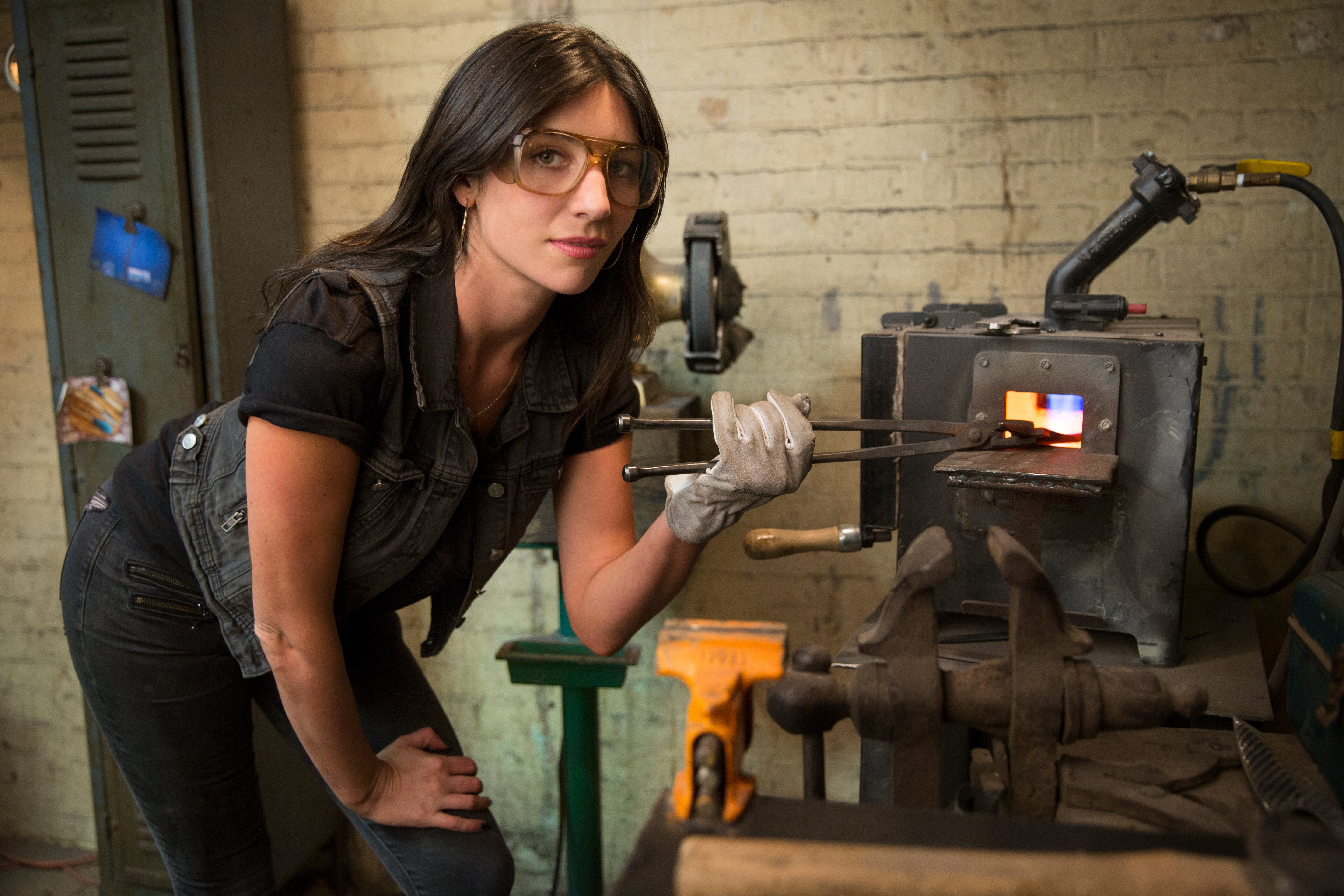 Chelsea Miller by the forge with safety glasses in her workshop